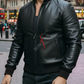 Man wearing a black leather jacket with a red logo on a city street.