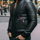 Man wearing a black leather jacket with a brand logo on a city street.