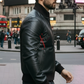 Man wearing a black leather jacket with a brand logo on a city street.