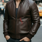 Man wearing a brown leather jacket with a brand logo on a city street.