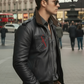 Man wearing a black leather jacket with a red logo on a city street