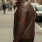 Man wearing a brown leather jacket with a brand logo on a blurred street background