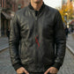 Man wearing a black leather jacket with a red logo on a city street.
