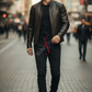 Man walking on a city street wearing a leather jacket and sunglasses.