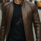 Man wearing a brown leather jacket and black t-shirt with a logo, standing on a blurred city street.