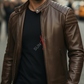 Man wearing a brown leather jacket and sunglasses with a blurred city street background