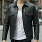 Man wearing a black leather jacket over a white shirt with red text on a city street.