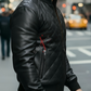 Man wearing a black leather jacket with a brand logo on a city street
