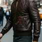 Man wearing a brown leather jacket with a brand logo on a city street.