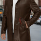 Brown leather coat worn by a person on a blurred city street background