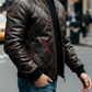 Man wearing a brown leather jacket with a brand logo on a city street