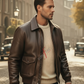 Man wearing a brown leather jacket and white sweater with red text on a city street.