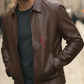 Man wearing a brown leather jacket with a brand logo on a blurred street background