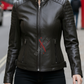 Woman wearing a black leather jacket with a brand logo on a city street.