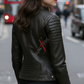 Woman wearing a black leather jacket with a brand logo on a city street.