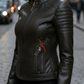 Woman wearing a black leather jacket with a brand logo on a city street.